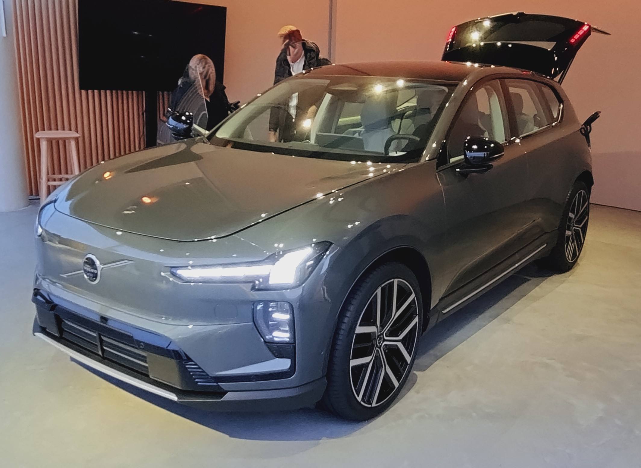 A grey Volvo EX60 on an indoor display stand, front three-quarter view, with its tailgate open