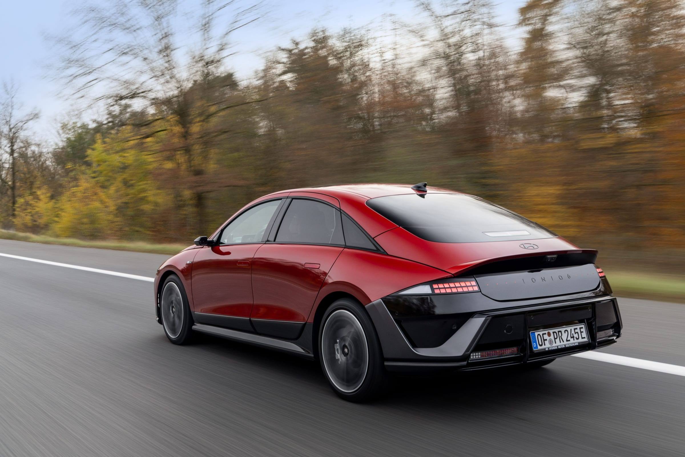 Rear three-quarter view of a red Hyundai Ioniq 6 N Line on a motorway, showing the black lower body and ducktail rear spoiler