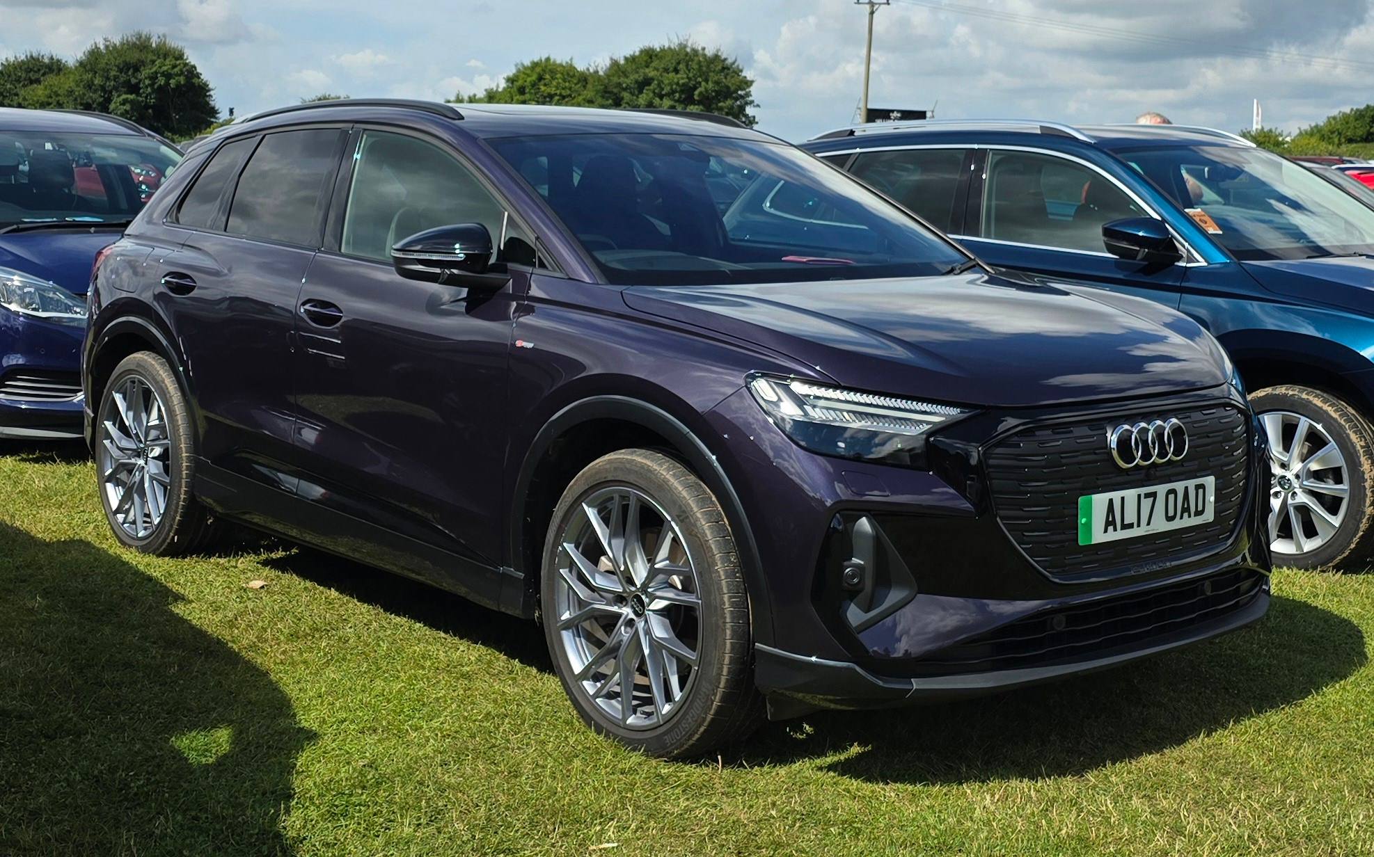 A dark purple Audi Q4 e-tron parked on grass among other cars, front three-quarter view