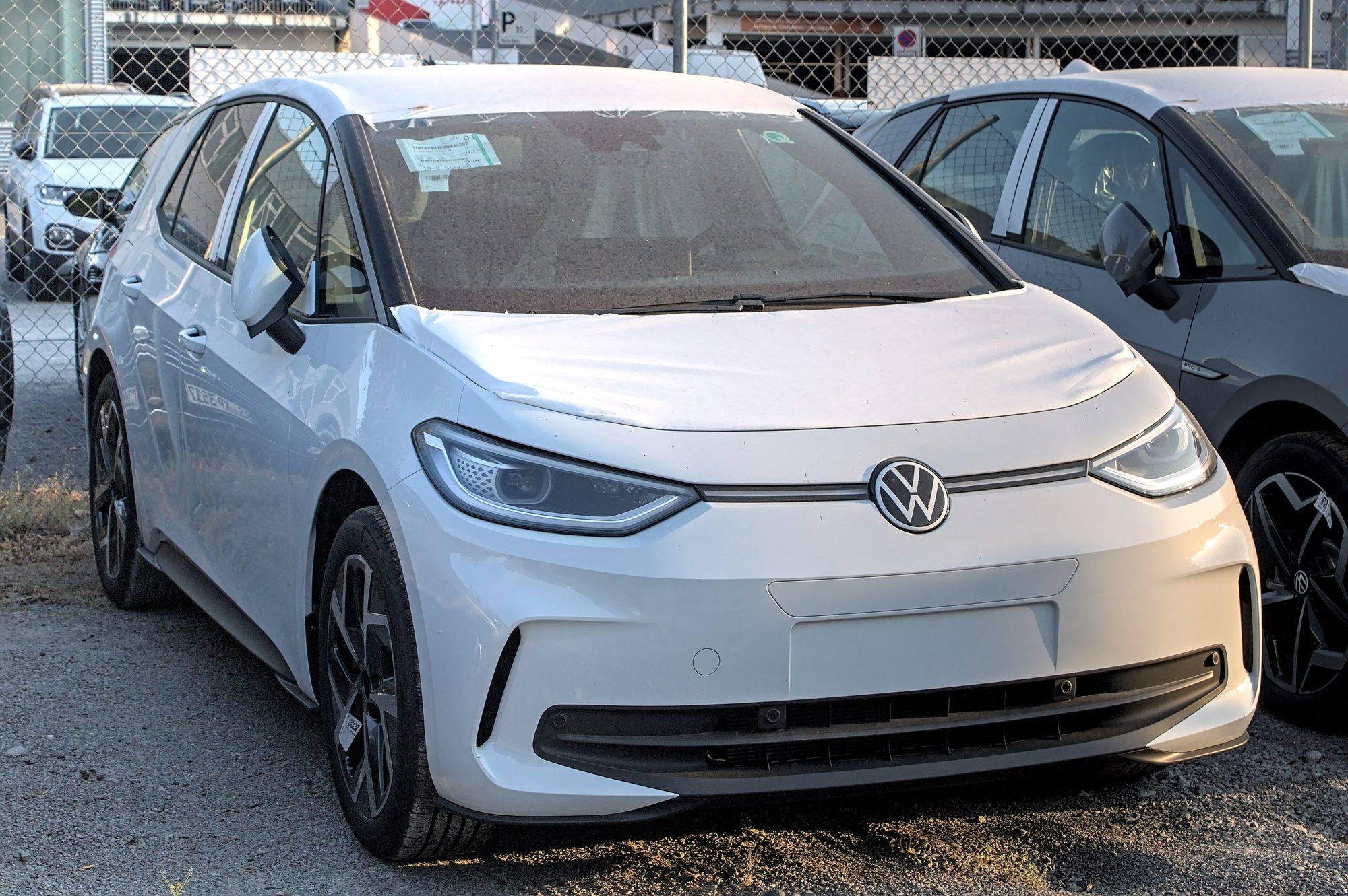A white Volkswagen ID.3 with protective film on its bonnet, parked behind a wire fence