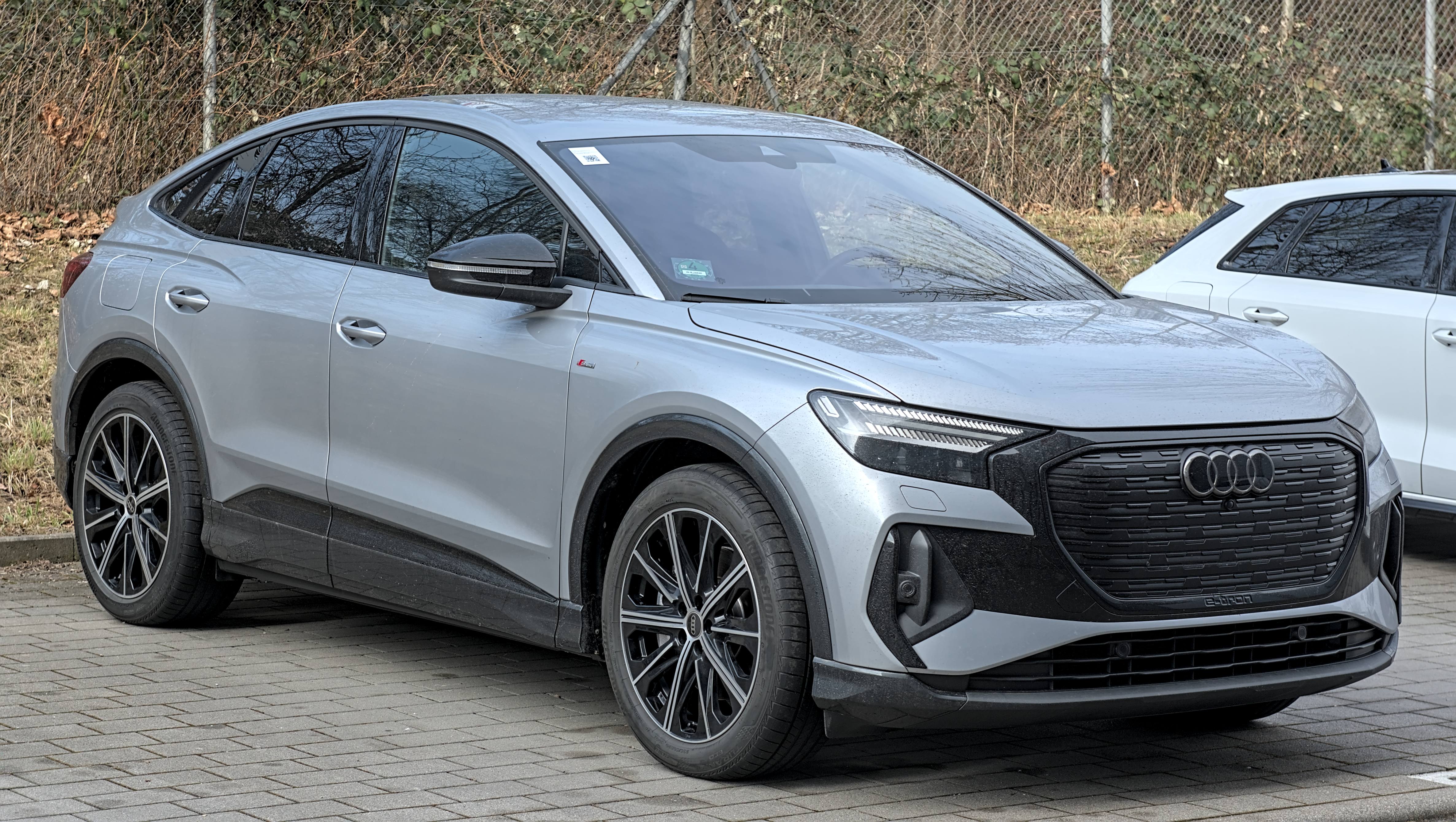 A silver Audi Q4 Sportback e-tron with a sloping roofline parked in a car park, front three-quarter view