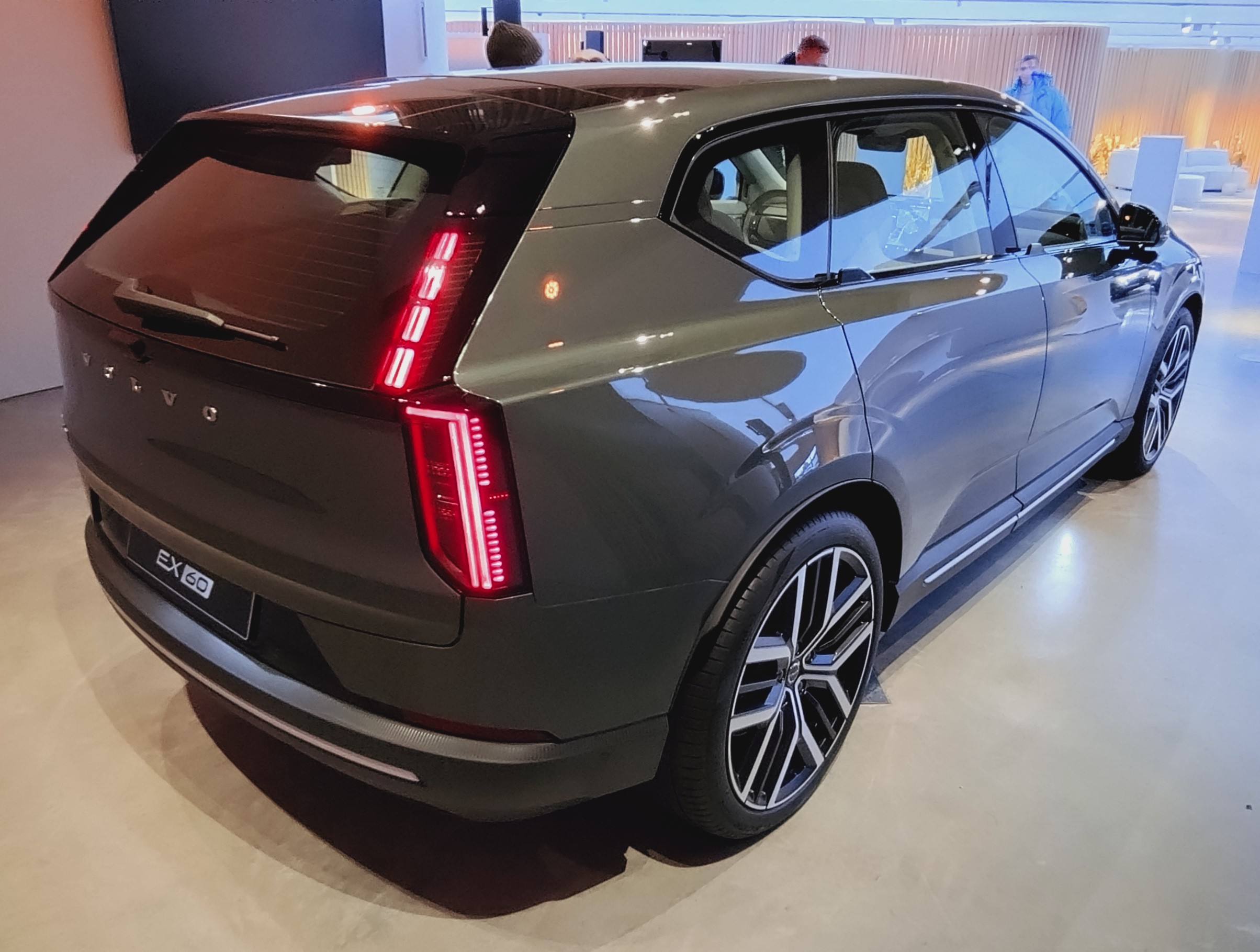 Rear three-quarter view of a grey Volvo EX60 indoors, showing its vertical tail lights and EX60 badge