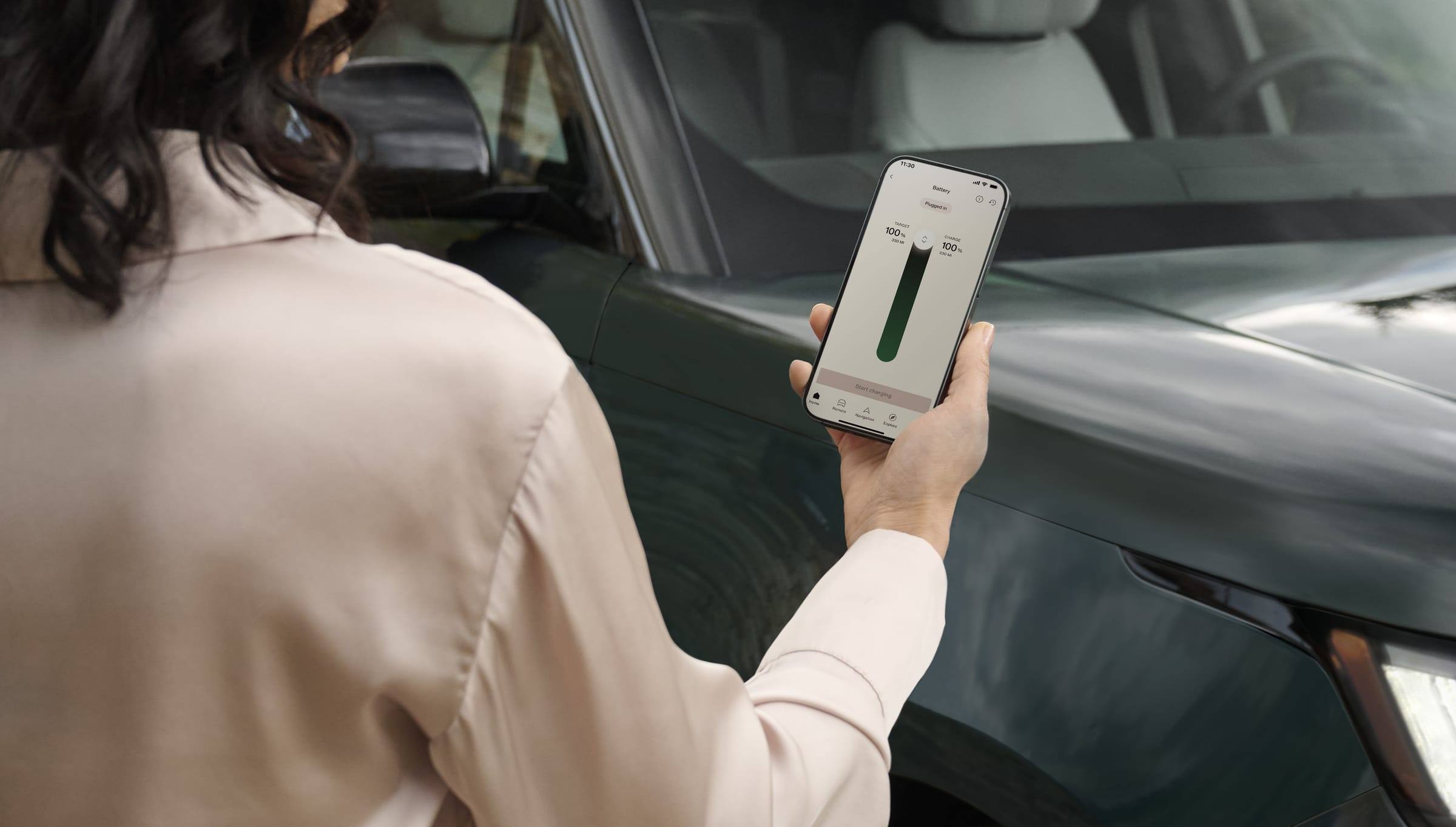 A person holding a smartphone showing a charging screen beside a dark green Range Rover Electric