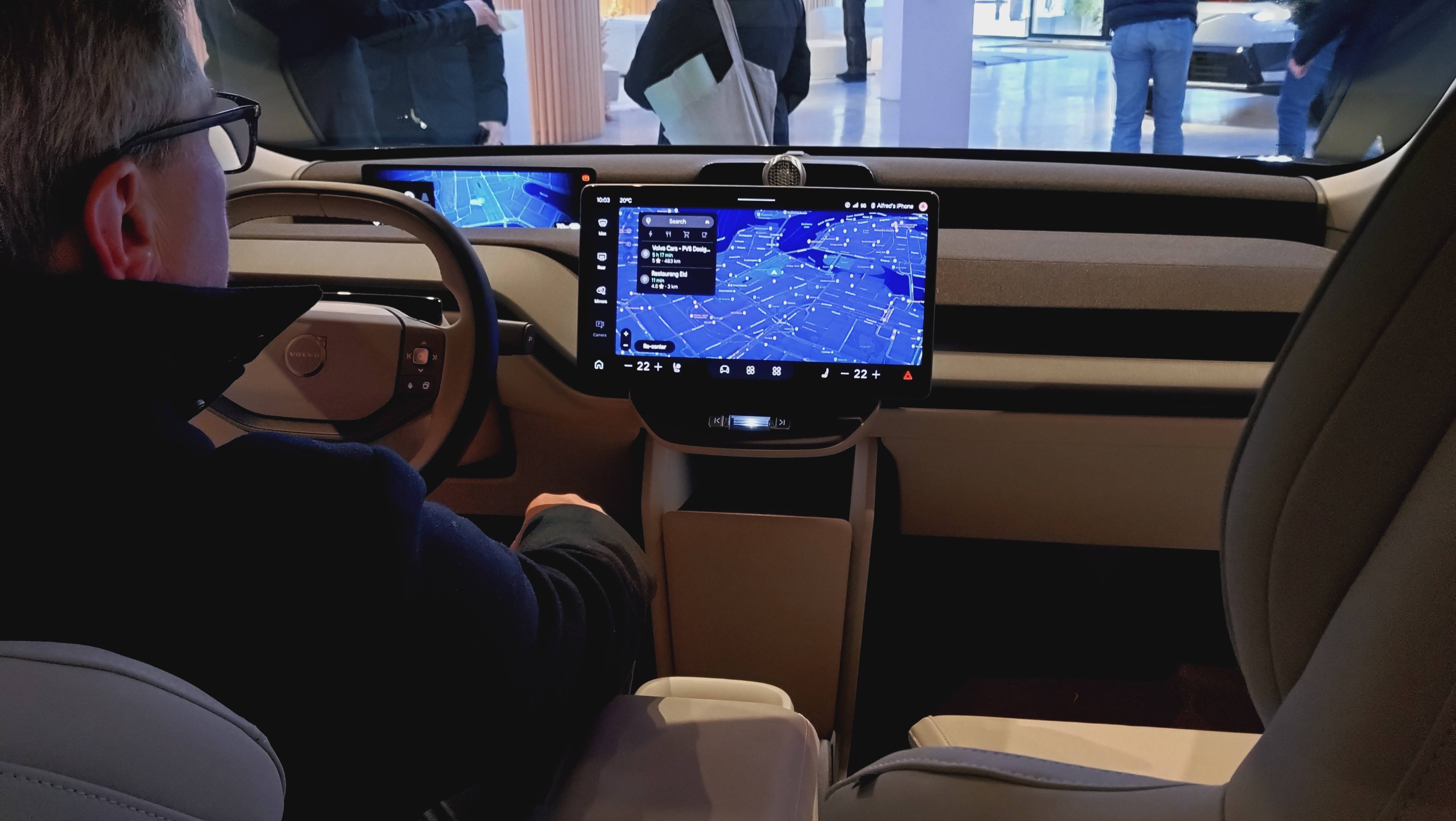 A visitor sits in the driver's seat of a Volvo EX60, with a large central touchscreen showing a map