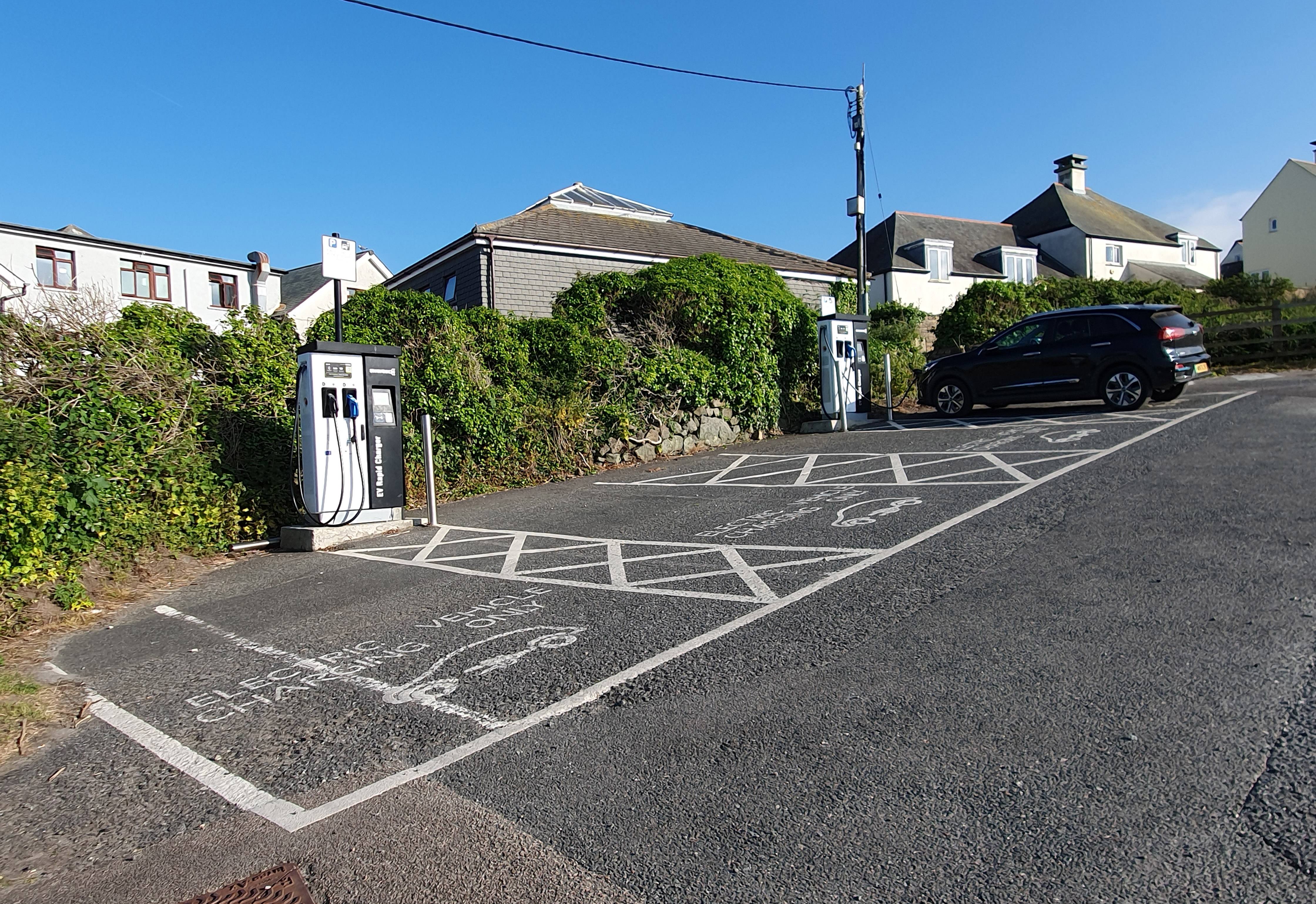 A row of electric car charging points in a seaside town car park, with parked cars
