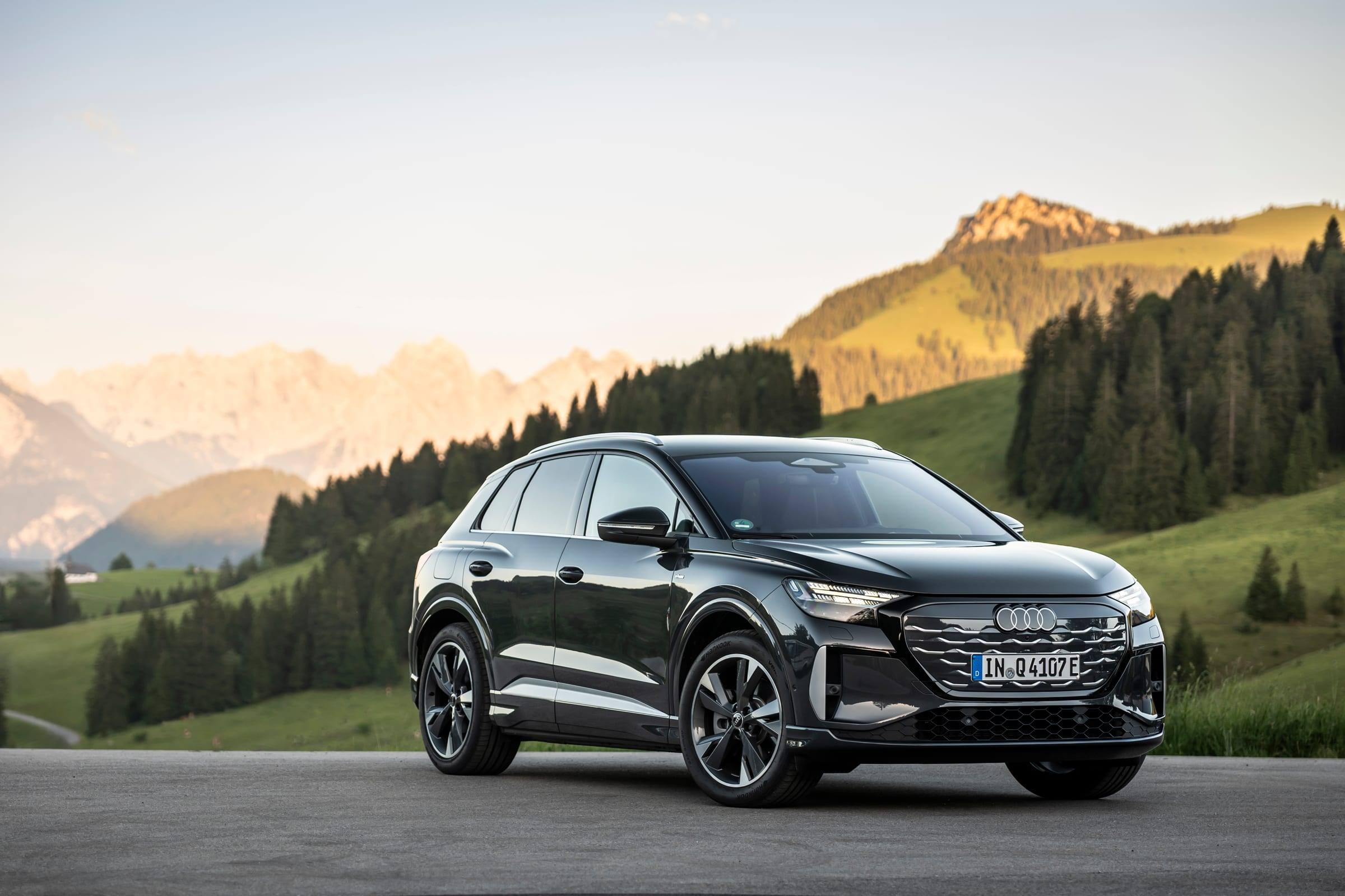 A dark grey updated Audi Q4 SUV e-tron parked in front of an alpine valley, seen from the front three-quarter view