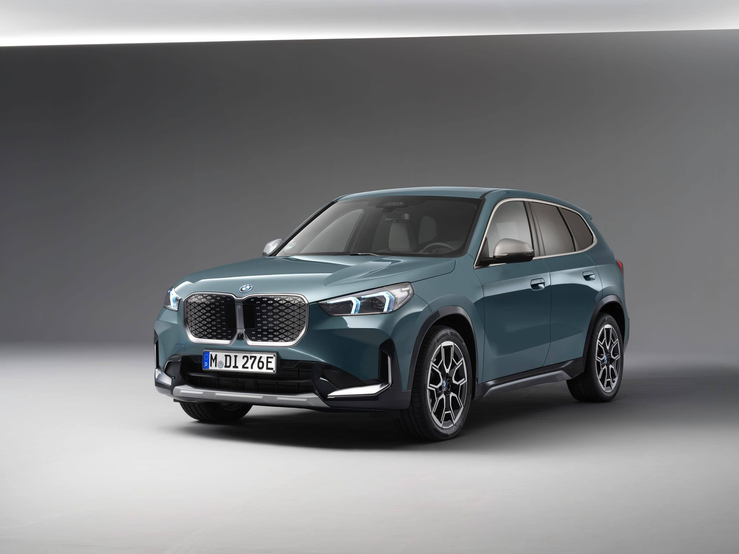 Blue-grey BMW iX1 eDrive20, front three-quarter view, in a grey studio