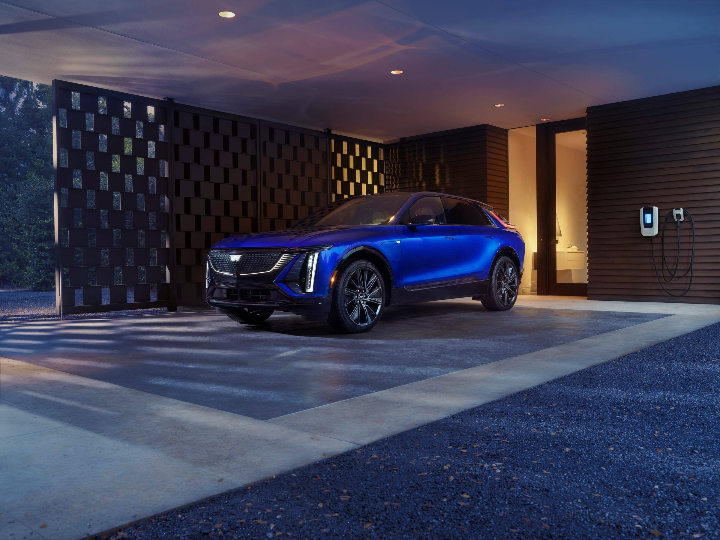 Blue Cadillac Lyriq, front three-quarter view, parked under a modern carport at dusk
