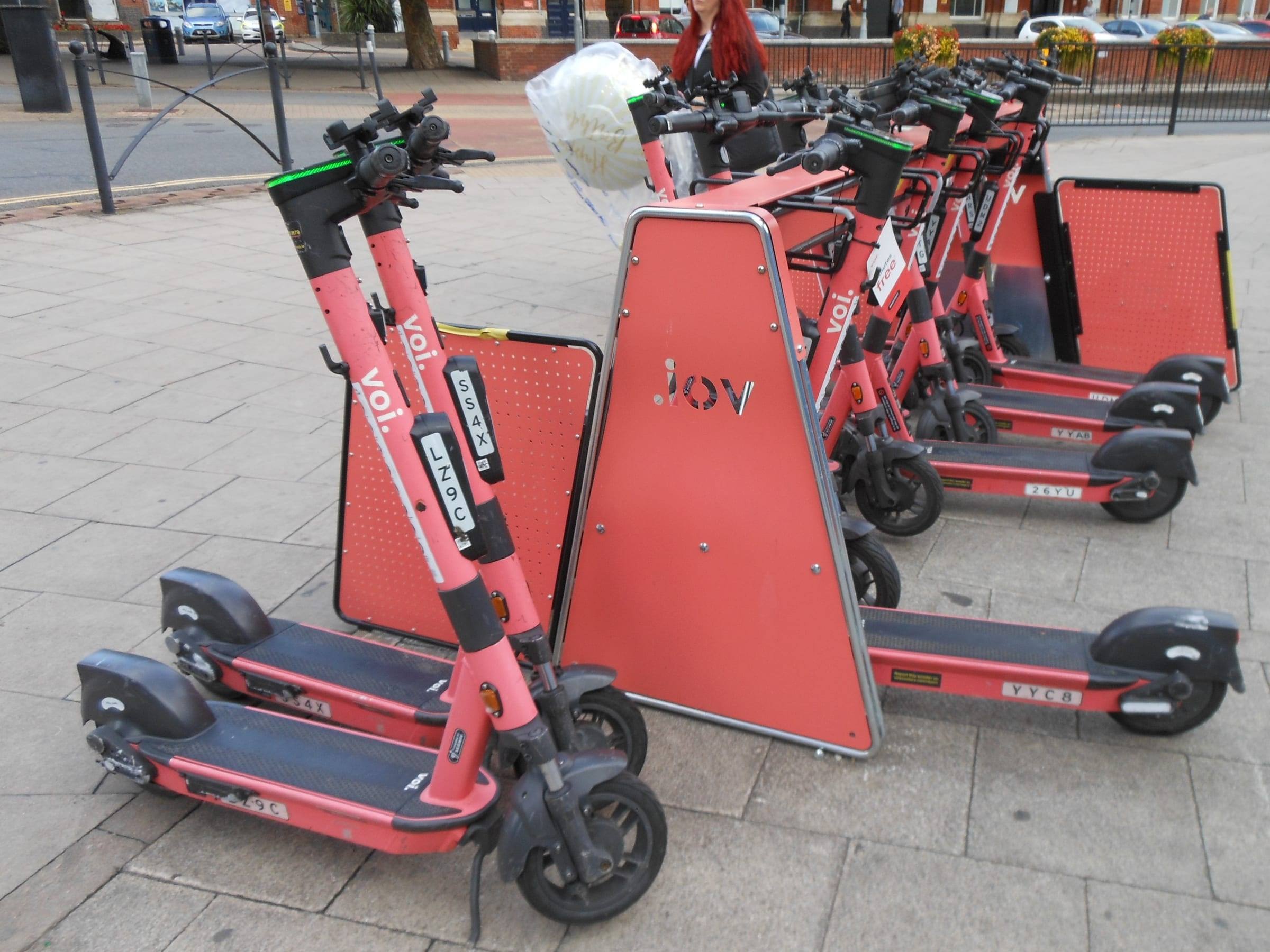 Rental electric scooters parked in a hire and charging bay outside a railway station in Portsmouth