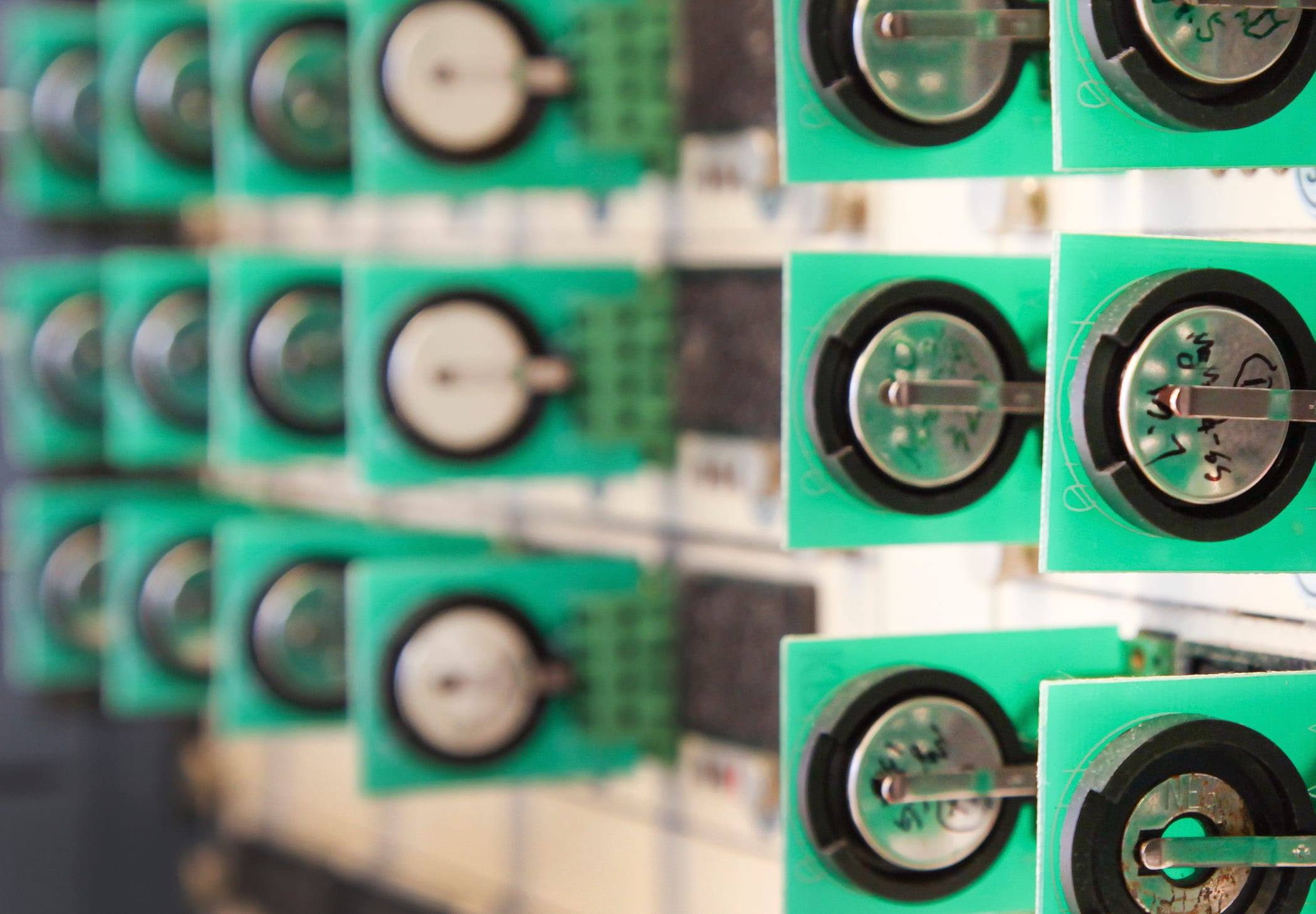 Rows of small coin-type test battery cells mounted on green circuit boards in a laboratory rack