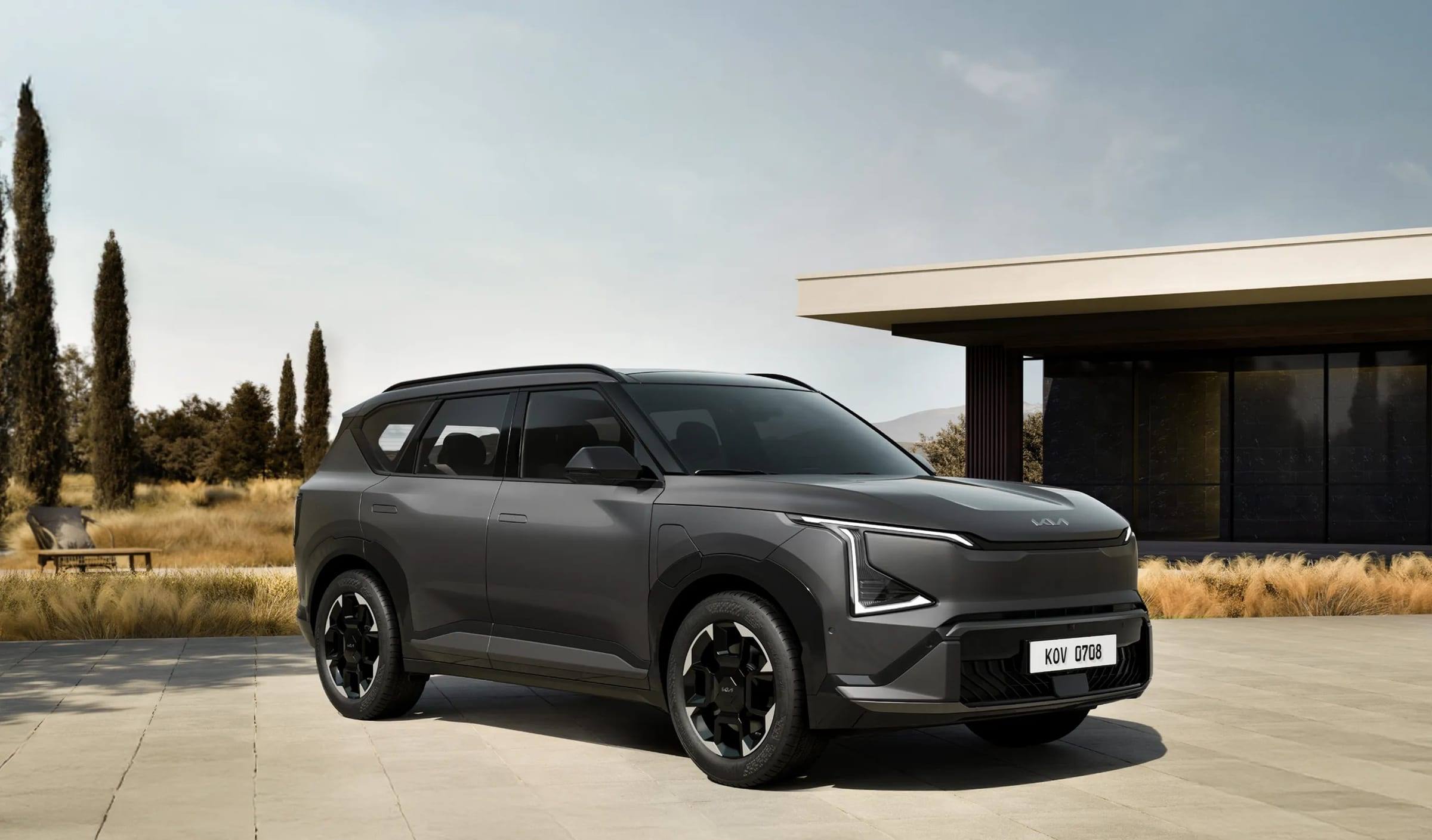 Dark grey Kia EV5, front three-quarter view, parked outside a modern house