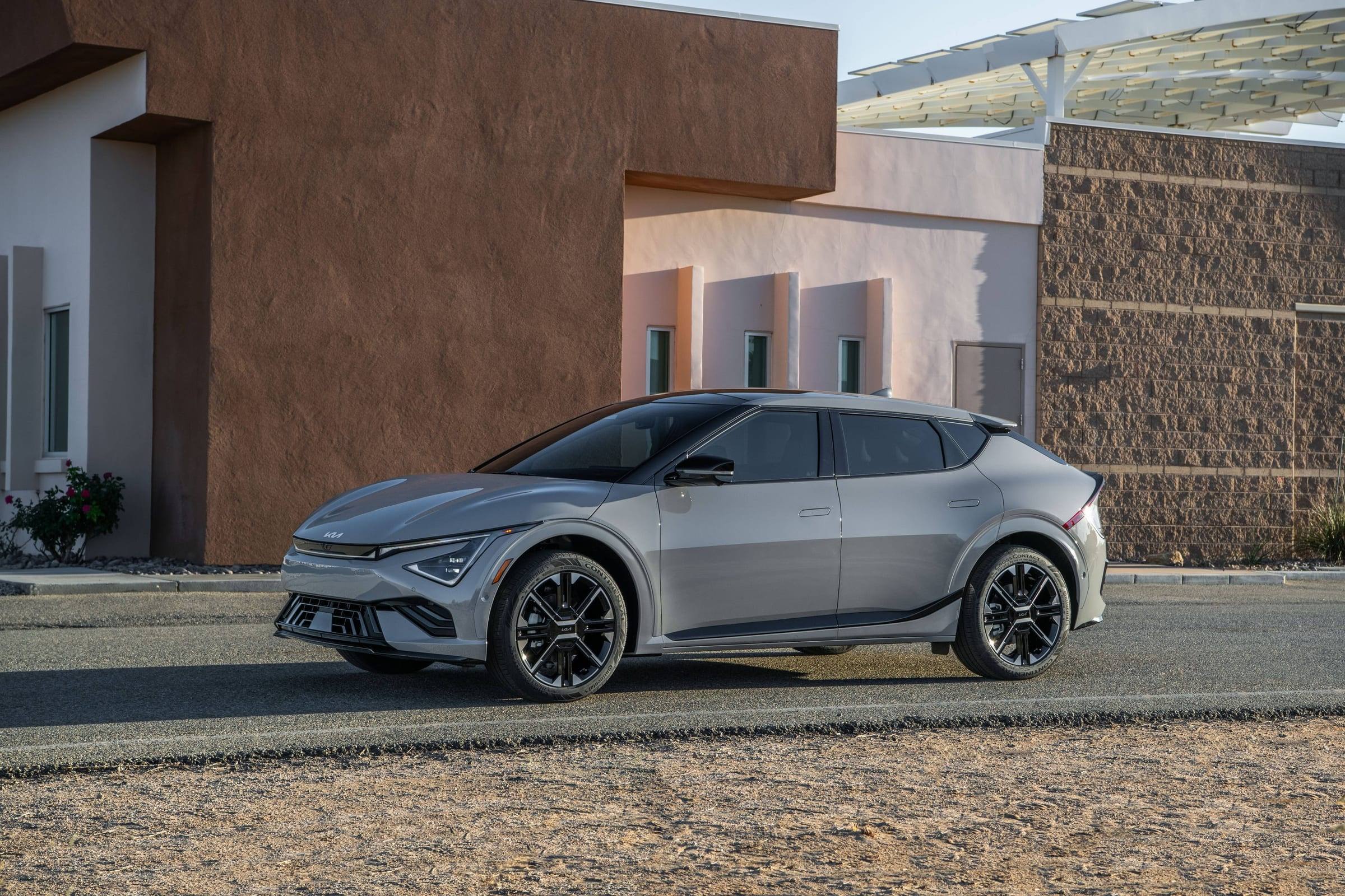 Silver-grey 2026 Kia EV6, front three-quarter view, parked beside a modern building in the desert