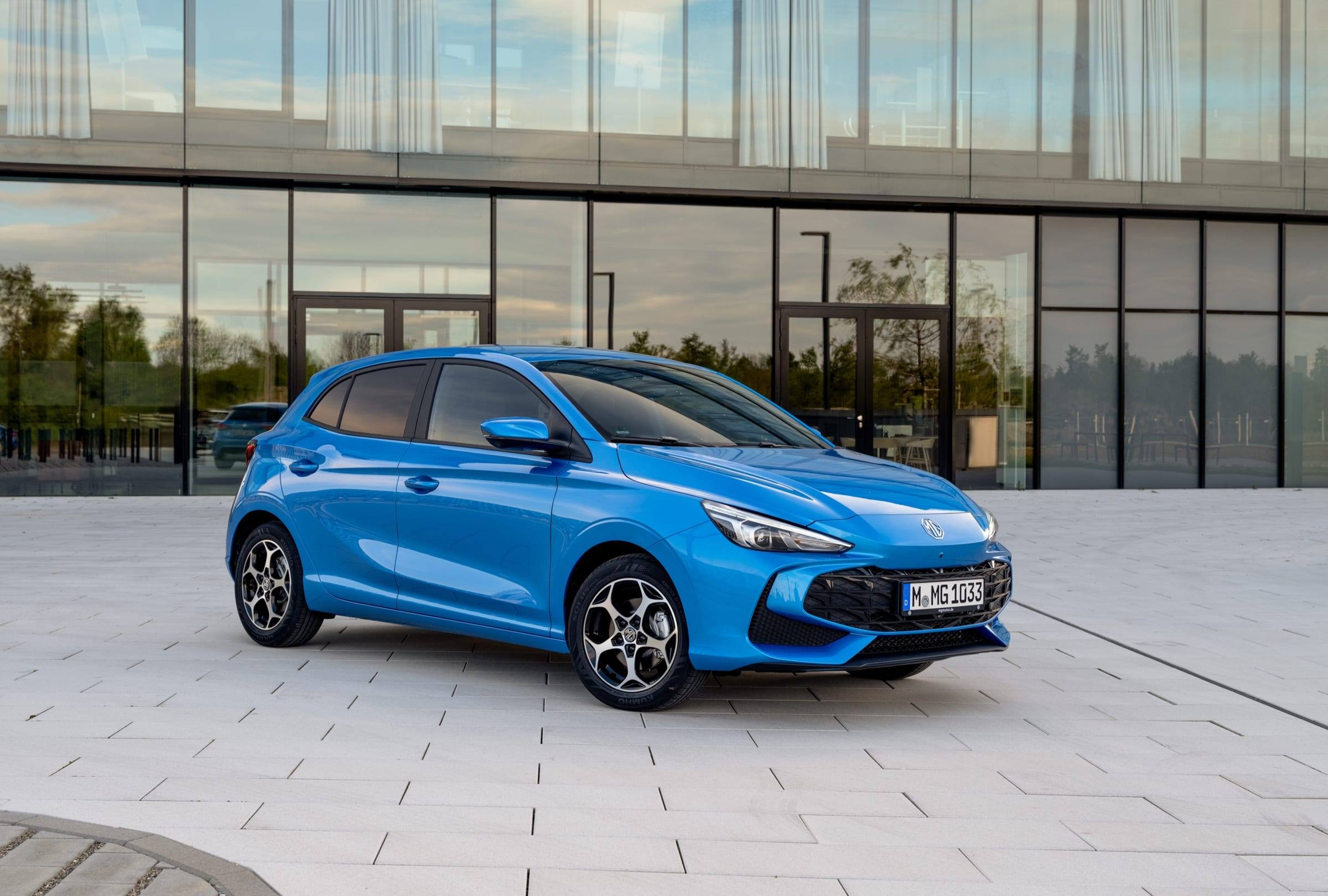Blue MG3 Hybrid+ Luxury, front three-quarter view parked in front of a glass office building