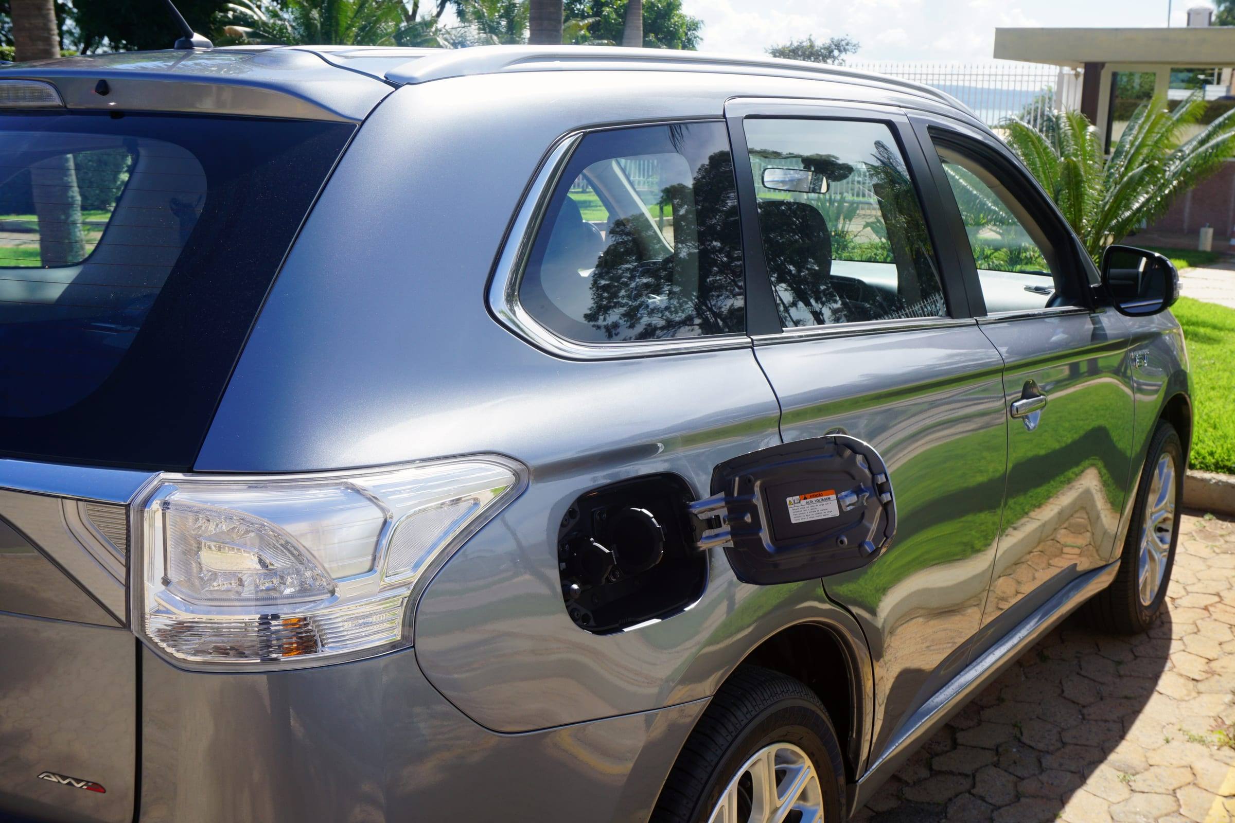 The rear quarter of a grey Mitsubishi Outlander PHEV with its charging flap open, showing the charging socket