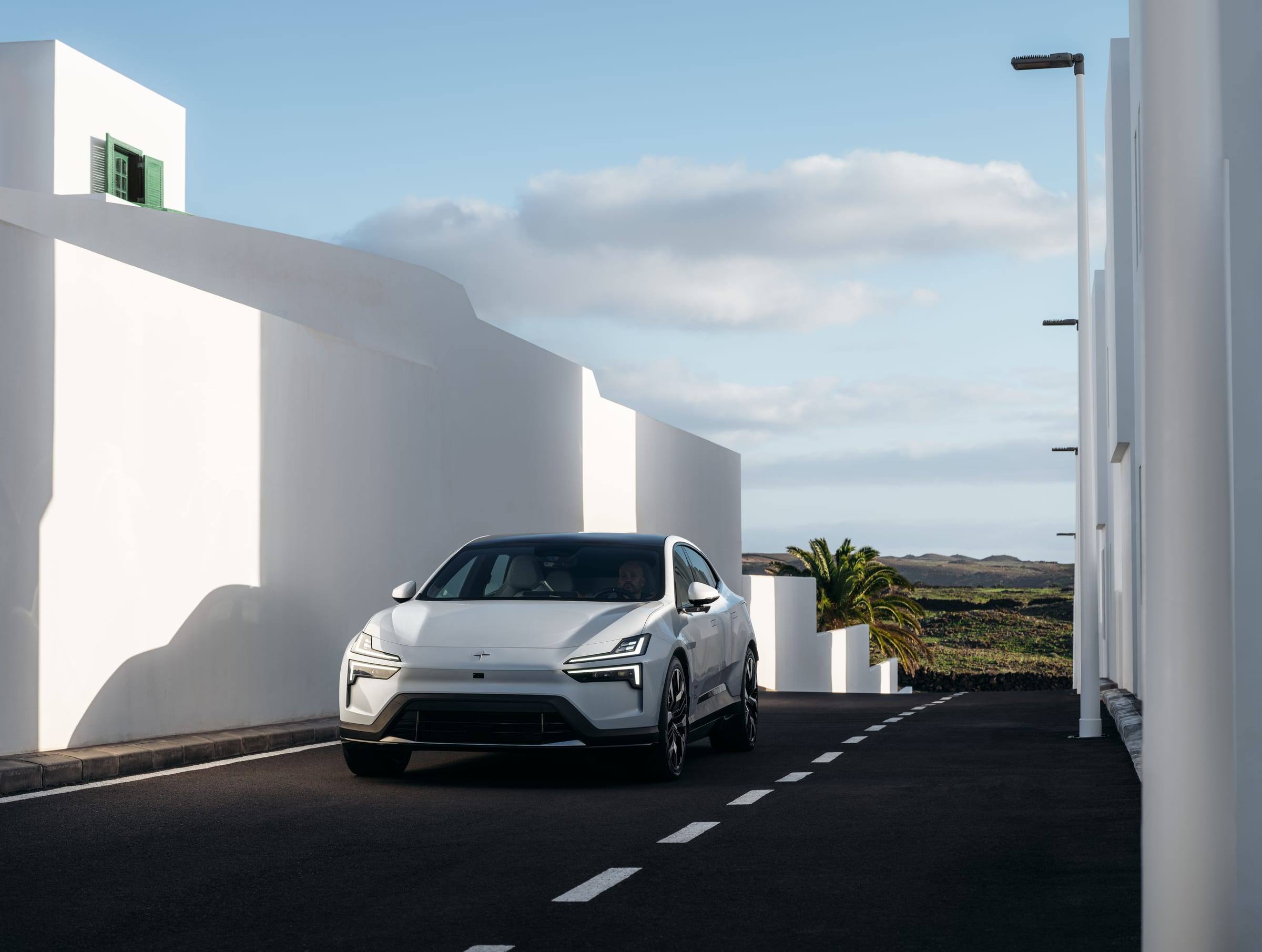 A white Polestar 4 coupé on a road between white-walled buildings, seen from the front three-quarter view