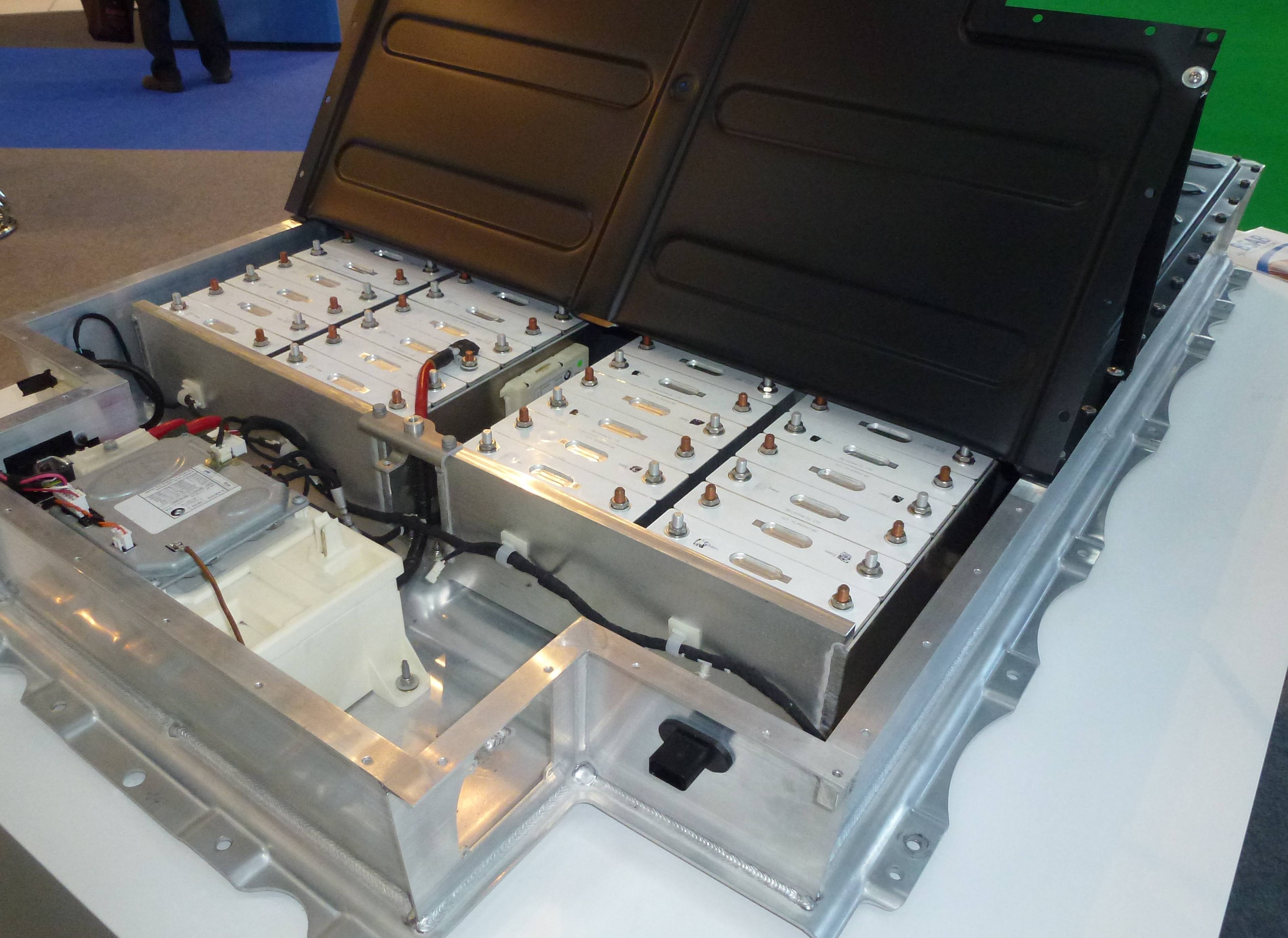 An opened lithium-ion battery pack for a BMW i3 on display at a trade show, showing rows of battery modules