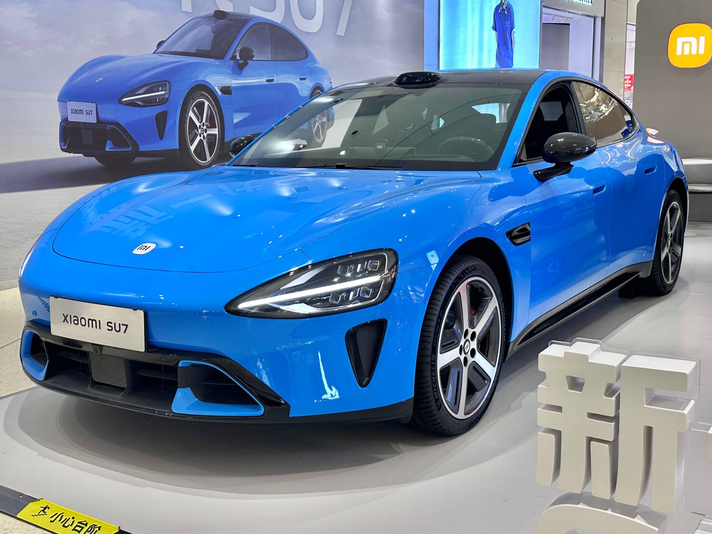 Blue new-generation Xiaomi SU7, front three-quarter view, on display in a showroom